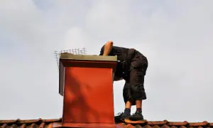 Pracownik na dachu wykonuje uszczelnianie komina, dbając o jego szczelność i bezpieczeństwo.