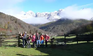 Grupo de senderistas posa junto a un cercado de madera en la ruta Soto de Sajambre-Vegabaño, con montañas nevadas al fondo.