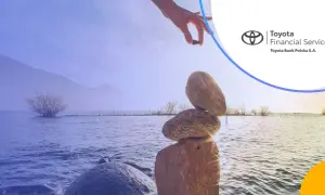 Równowaga kamieni na brzegu jeziora, ręka kładzie ostatni kamień. Logo Toyota Bank.