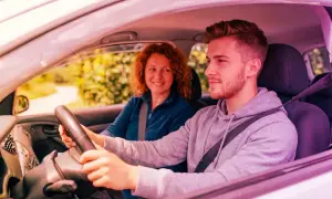 Giovane uomo guida, madre sorride. Ricorda che l'assicurazione auto deve essere intestata al proprietario per la massima tranquillità.
