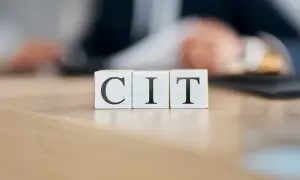 Trzy kostki z literami C, I, T układają się w napis CIT. W tle rozmyta postać pochylona nad dokumentami, sugerująca pracę nad podatkiem CIT.