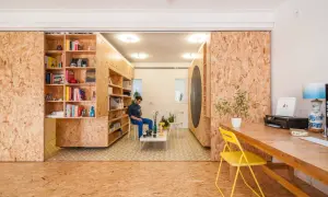 Ein Mann sitzt in einem Raum, der mit OSB-Platten für den Innenausbau gestaltet ist. Bücherregale und ein Schreibtisch sind ebenfalls aus OSB gefertigt.
