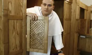 Ksiądz w białej albie otwiera kratkę konfesjonału, czekając, kiedy jest spowiedź w kościele.