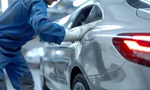 Un ouvrier en bleu vérifie la carrosserie d'une voiture argentée. Le prix de la carrosserie est une préoccupation pour de nombreux propriétaires.
