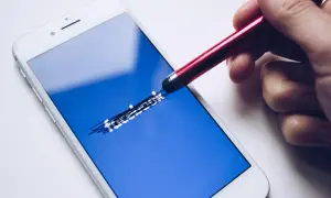Ręka rysuje stylusem na ekranie telefonu logo Facebooka. Zastanawiasz się, jak odzyskać konto Messenger?
