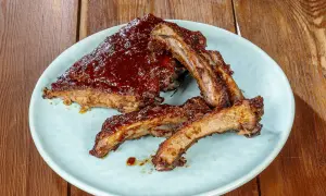 Succulente costine di maiale glassate con salsa barbecue, servite su un piatto azzurro su un tavolo di legno.