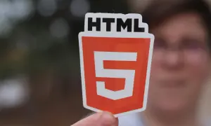 Osoba trzyma naklejkę z logo HTML5, symbolizującą wiedzę, jak utworzyć stronę html.