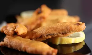 Beignets de sardines dorés et croustillants, servis avec des rondelles de citron sur une assiette noire.