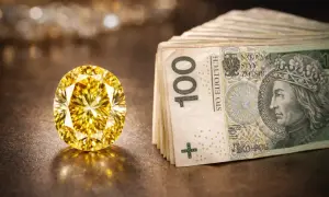 Olśniewający, duży, żółty diament lśni obok stosu banknotów 100-złotowych.