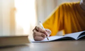 Main d'une personne écrivant dans un cahier, peut-être pour l'archive des noms de famille algériens.