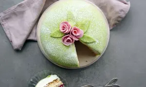 En vacker prinsesstårta med grönt marsipanlock, rosa rosor och blad. Ett stycke är uppskuret, perfekt för ett prinsesstårta recept.