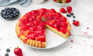 Ein köstlicher obstboden mit erdbeeren, bedeckt mit glänzendem Gelee. Daneben Blaubeeren und frische Erdbeeren.
