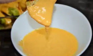 Un totopo cubierto de queso fundido cremoso se sumerge en un tazón de queso.