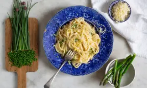 En tallrik krämig pasta limone, toppad med riven ost och persilja. Bredvid finns färsk gräslök och sparris.