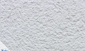 Nahaufnahme einer weißen, strukturierten Wand, die zeigt, wie man eine Wand verputzt. Das Korn ist unregelmäßig und erzeugt eine interessante Textur.