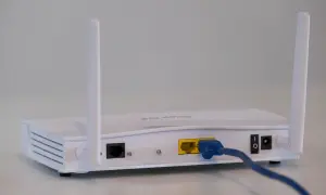 Biały router z dwiema antenkami. Widoczne porty LAN, zasilania i przycisk włączania. To urządzenie, czym się różni modem od routera, rozdziela internet.