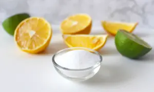 Una ciotola di cristalli bianchi, che ricordano la struttura dell'acido citrico, circondata da spicchi di limone e lime freschi.