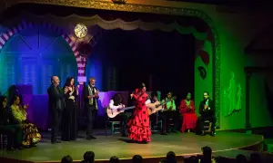 Una bailarina de **tango flamenco** con un vestido rojo y lunares negros cautiva en el escenario, acompañada por guitarristas y cantantes.