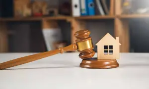 Richterhammer und Holzhaus-Modell auf einem Tisch, symbolisch für ein Immobilien-Bieterverfahren.