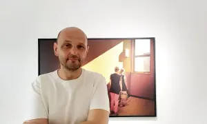 Krzysztof Gołuch obok swojego obrazu z kobietami niosącymi wiadra w świetle.