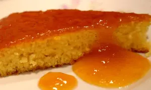 Una fetta di torta senza glutine, soffice e dorata, coperta da una lucida glassa all'arancia.