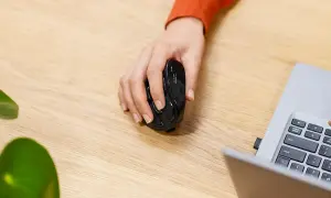 Mano sujetando un ratón negro, listo para usarlo y desbloquear el ratón del portátil.
