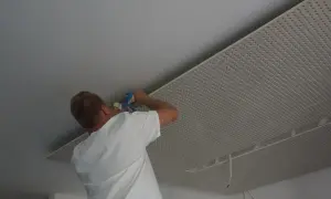 Mężczyzna montuje płyty karton gips na suficie w nieogrzewanym domu.