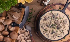 Cremige Rahmchampignons in einer Pfanne, daneben frische Champignons, Kräuter, Zitrone und Gewürze. Ein leckeres Rahmchampignons Rezept zum Nachkochen.
