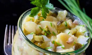 Ein köstlicher Kartoffelsalat ohne Mayo, mit Gurkenstücken und frischem Schnittlauch garniert, serviert in einem Glas.