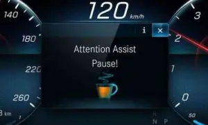 Il display mostra "Attention Assist Pause!" con una tazzina di caffè, indicando come funziona il rilevatore di stanchezza Volkswagen: suggerisce una pausa.