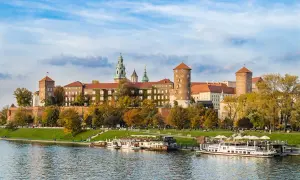 Zamek Królewski na Wawelu, majestatyczna budowla nad Wisłą, otoczona jesienną zielenią i błękitem nieba.
