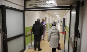 Korytarz szpitalny z tabliczką "Klinika Chirurgii Ortopedyczno-Urazowej", pacjenci i lekarka.