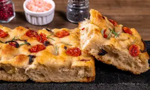 Złocista focaccia z pomidorkami koktajlowymi i rozmarynem, z widocznym puszystym wnętrzem.