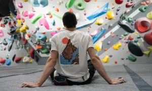 Mann sitzt vor einer Boulderwand mit bunten Griffen. Er ist bereit, besser klettern zu lernen.