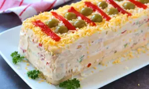Pastel de atún con pan de molde, decorado con pimientos rojos, aceitunas y huevo rallado. ¡Una delicia!