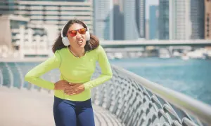 Une coureuse en tenue de sport, écouteurs aux oreilles, souffre d'un point de côté aigu en pleine course le long d'une promenade urbaine.