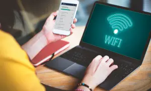 Osoba korzysta z telefonu i laptopa, na ekranie którego widnieje symbol Wi-Fi. Możliwość wi-fi calling Orange ułatwia pracę zdalną.