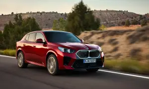 Czerwone BMW X2 2025 pędzi po pustynnej drodze, otoczone suchymi wzgórzami i drzewami.