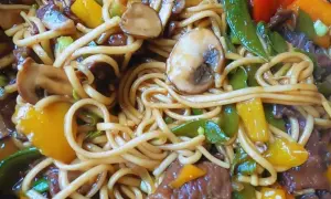 Pyszny makaron chow mein z wołowiną, pieczarkami, papryką i groszkiem cukrowym w sosie.