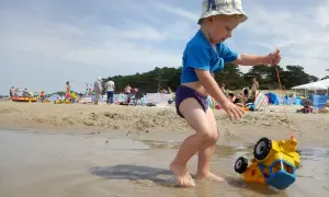 Chłopiec ciągnie zabawkowe auto po plaży w Darłowie. To świetne darłowo atrakcje dla dzieci, gdzie można się bawić w wodzie i piasku.