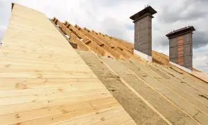 Costruzione di un tetto con coibentazione in lana di roccia e pannelli in legno. Due camini in muratura emergono dalla struttura.