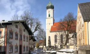 Winterliche Szene in Oberammergau mit der Pfarrkirche St. Peter und Paul. Die Fassadenmalerei der Häuser und die schneebedeckten Wege lassen die Vorfreude auf die passionsfestspiele oberammergau spüren.