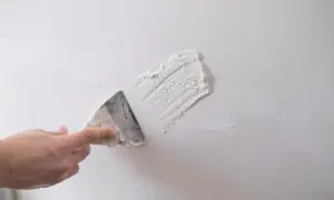 Dłoń z kielnią nakłada gips szpachlowy na białą ścianę.