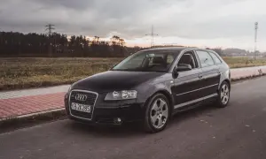 Czarne Audi A3 2009 na tle zachodzącego słońca i linii energetycznych.