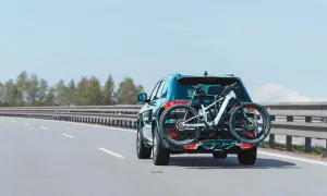 Un turismo transporta una bicicleta de montaña en un portabicicletas trasero. La carga sobresale considerablemente, pero es una forma común de llevar equipo deportivo.
