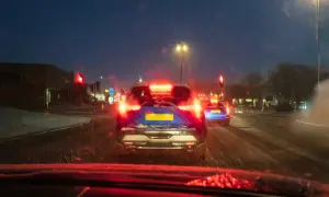 Noche de nieve, luces rojas de freno y un coche azul con matrícula amarilla. El asfalto mojado y la baja visibilidad aumentan el riesgo de derrape coche.