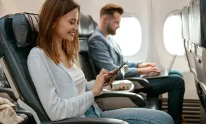 Kobieta i mężczyzna w samolocie. Ona korzysta z telefonu, on pracuje na laptopie. Tak działa tryb samolotowy, pozwalając na używanie urządzeń elektronicznych.