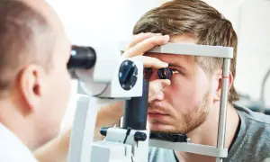 Lekarz wykonuje badanie dna oka młodego mężczyzny przy użyciu specjalistycznego sprzętu.
