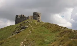 Kamienny zamek na szczycie zielonych gór w Ukrainie, pod burzliwym niebem.