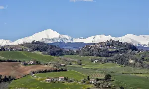 Paesaggio collinare con un borgo in cima, montagne innevate sullo sfondo. Un tranquillo scorcio del fermo provincia.